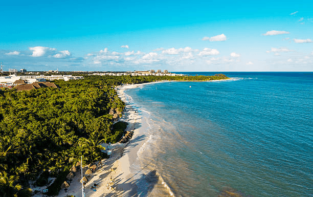 Aerial view of a long white-sand beach with palapas between jungle and turquoise sea