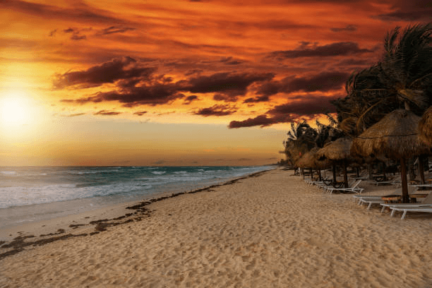 Thatched palapa umbrellas on a beach under a fiery orange sunset